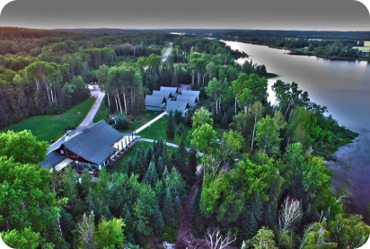 Aerial view of Elk Lake Lodge in summer. Green trees and the lodge overlooking large lake.