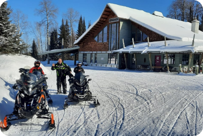 Snowmobilers in front of the Elk Lake Lodge. Sunny day, bright white snow.